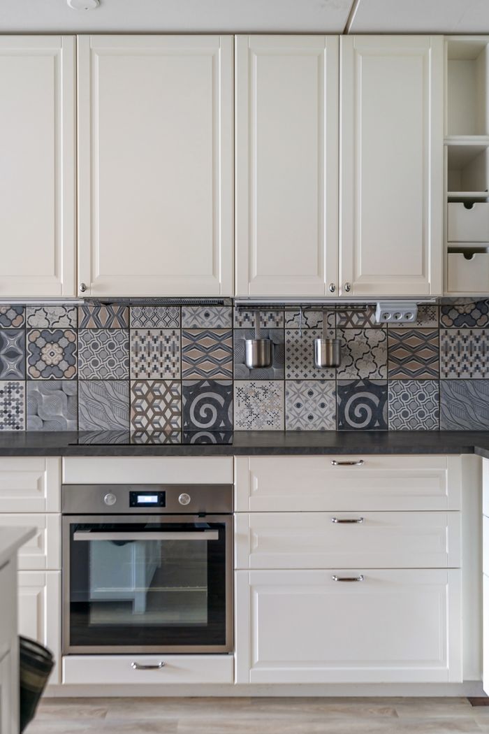 Elegant kitchen design featuring white cabinets and a patterned mosaic tile backsplash.